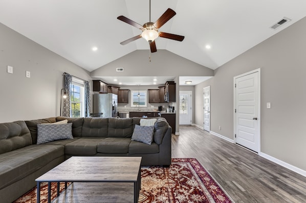 A spacious living room with a sectional sofa, a coffee table, and a ceiling fan. - Ft Campbell Cottage on Kendall (Clarksville)