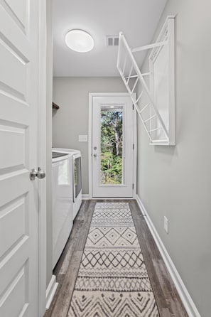 A hallway with a patterned rug, a white door leading to an outdoor area, and a white wall-mounted rack. - Ft Campbell Cottage on Kendall (Clarksville)