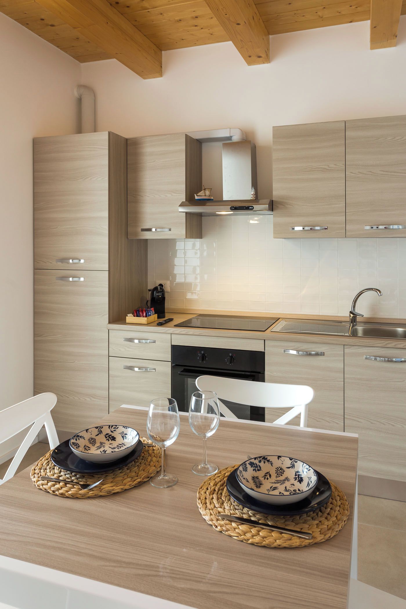 Eine moderne Küche mit Holzausstattung, einem Edelstahl-Spülbecken und einem Essbereich mit Tisch für zwei Personen.