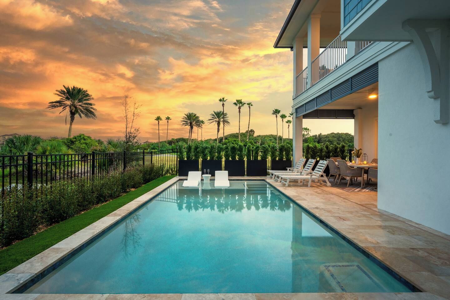 Una piscina con lettini, una zona pranzo e vista su palme al tramonto.