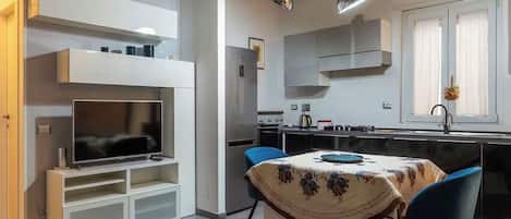 Una cocina moderna con electrodomésticos integrados, un comedor con mesa y sillas, y un televisor de pantalla plana.