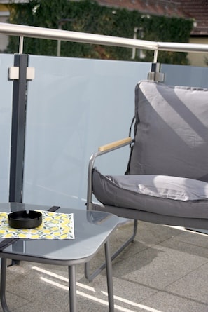 Een balkon met een metalen stoel en een kleine tafel met een asbak.