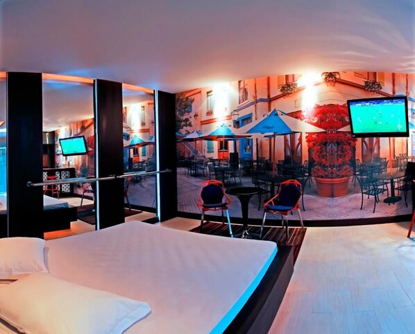 A hotel room with a bed, a TV, a seating area with chairs, and a mural of an outdoor scene. - Gran Motel Dubai by Drops (Caxias do Sul)