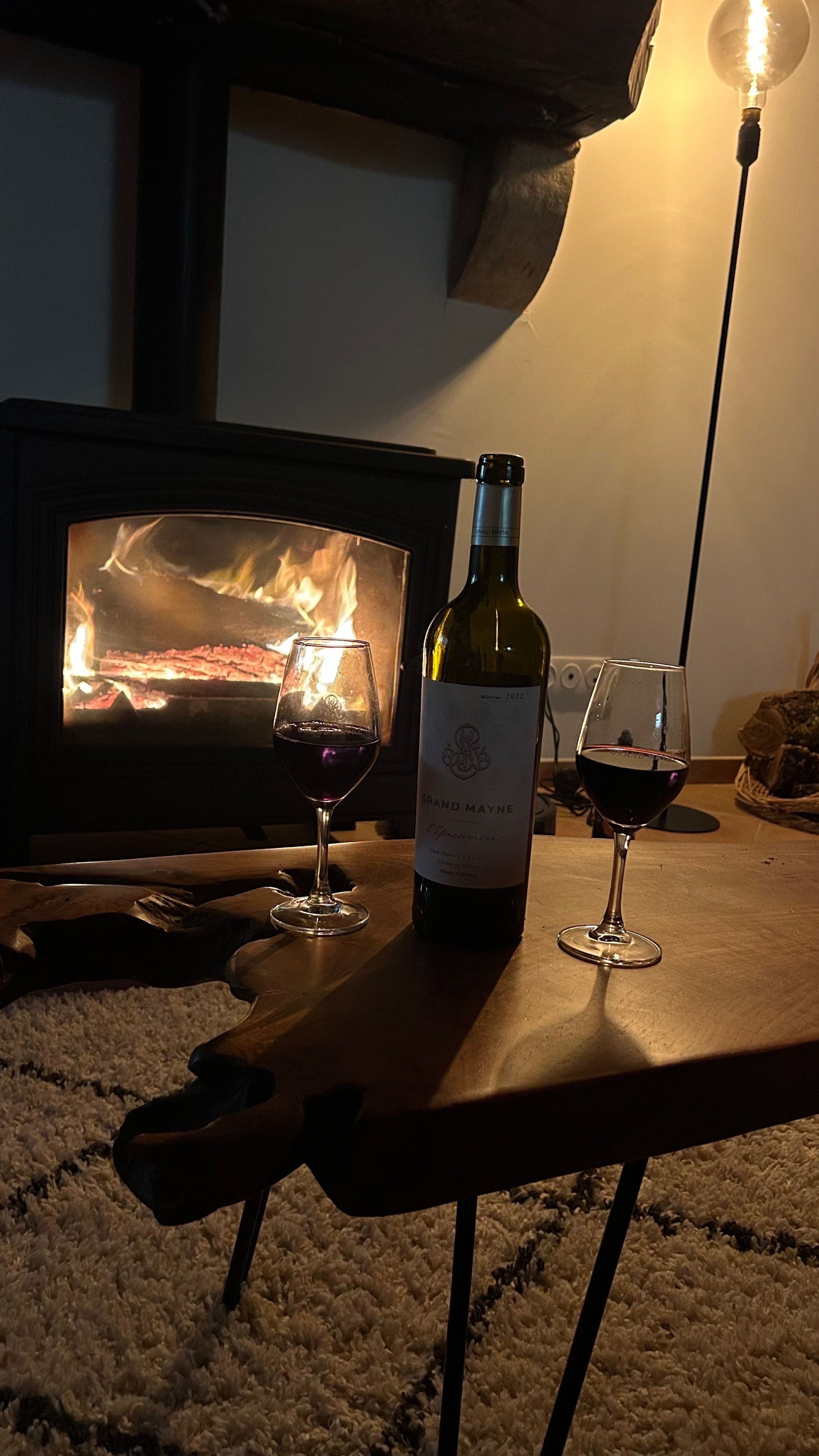 Una habitación acogedora con chimenea, una botella de vino y dos copas sobre una mesa.