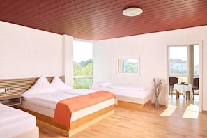 Una habitación de hotel con una cama grande, cabecera de madera, una mesita y vistas al exterior.