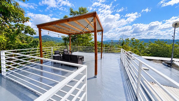 A rooftop terrace with a pergola, seating area, and railing.