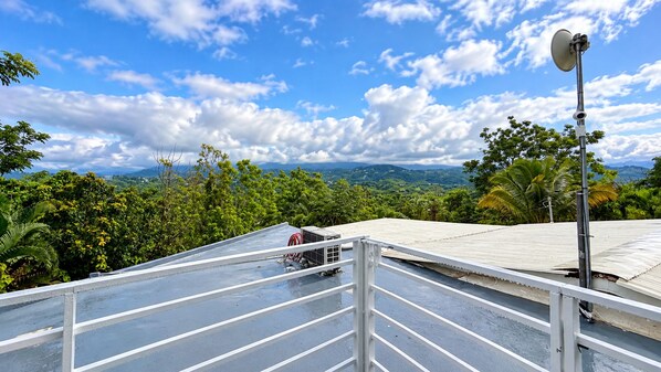 A rooftop with a metal railing, a satellite dish, and a view of a green landscape with trees and mountains. - Escape to our mountaintop retreat Apt.2 (Aguas Buenas)