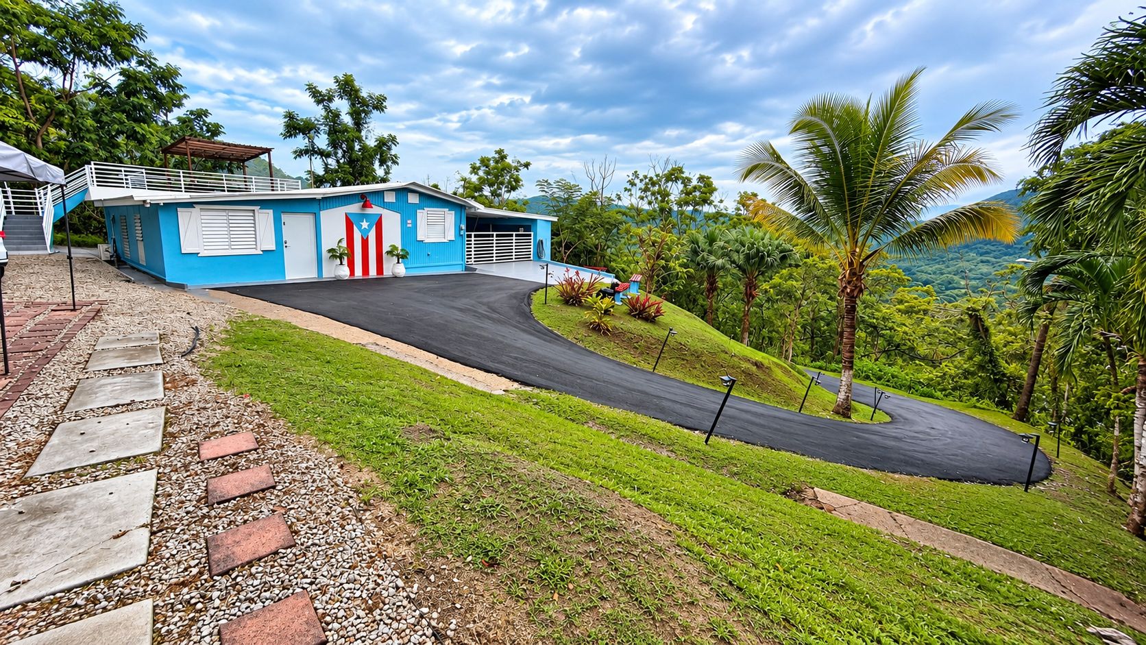 A blue building with a flag, a paved driveway, and a grassy area with palm trees.