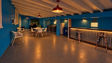 A room with a blue wall, a dining area with a table and chairs, a bar area with stools, and a ceiling with exposed beams.