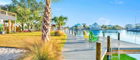 A wooden boardwalk leading to a waterfront with a clear view of the water, a pool, and a building with a blue roof.