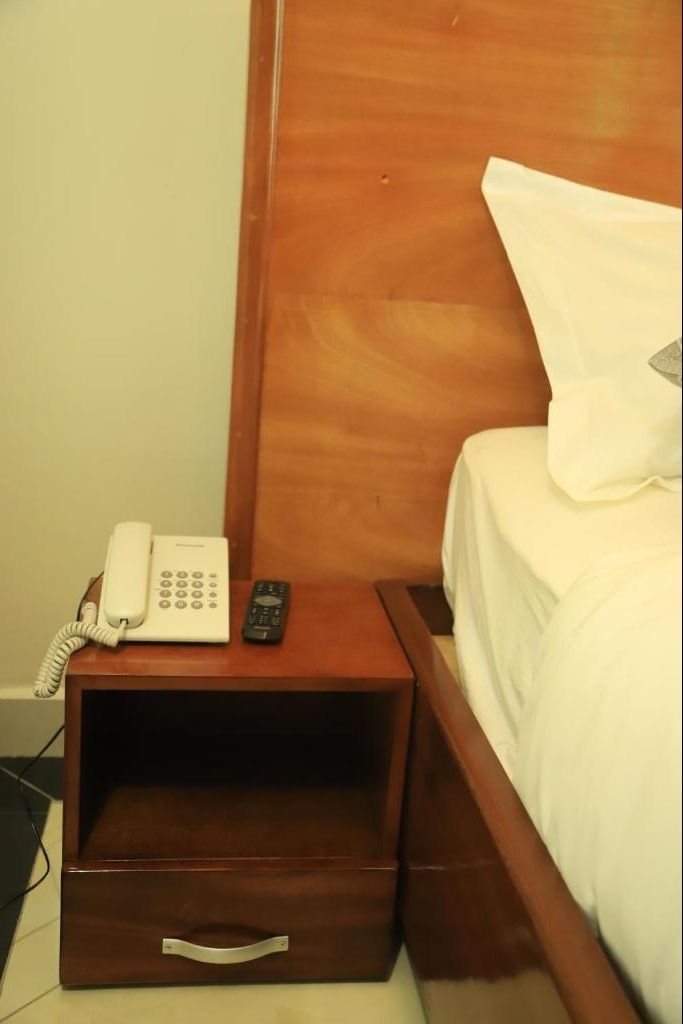 Une table de chevet en bois avec un téléphone blanc et une télécommande.