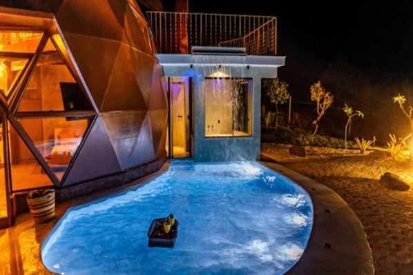Un bâtiment moderne à la structure en verre, doté d’un jacuzzi et d’une petite cascade décorative.