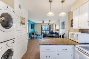 A modern kitchen with built-in appliances, a dining area with a view, and a laundry room. - Lani Kai 121🏖️ Walk to Beach Access + Bahama Bob’s | 2 Pools + BBQ Area (Gulf Shores)