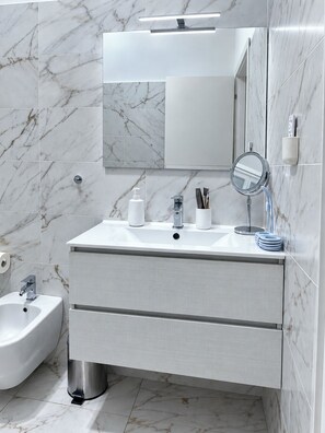 A modern bathroom with a marble backsplash, a large mirror, a sink with a faucet, a bidet, and a vanity with drawers. - Pavone House near the Duomo (Milano)