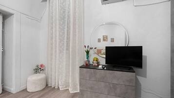 A modern bedroom with a grey dresser, a flat-screen TV, a small round mirror, and a white air conditioning unit on the wall.