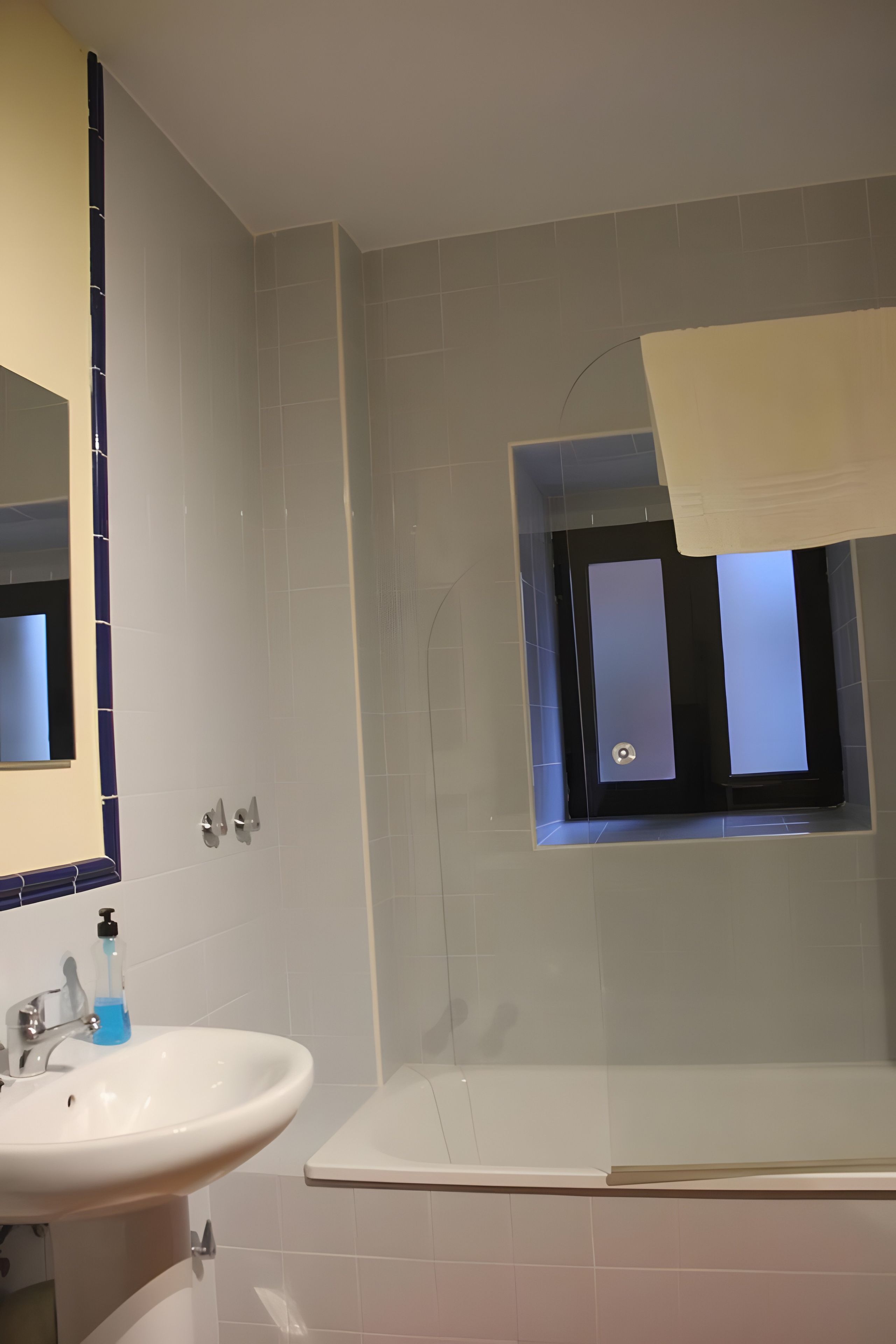 A bathroom with a white sink, a mirror, a shower, and a window with a view.