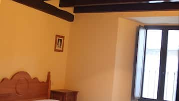 Une chambre à coucher avec un lit, une tête de lit en bois, une petite table de chevet et une fenêtre avec des stores.