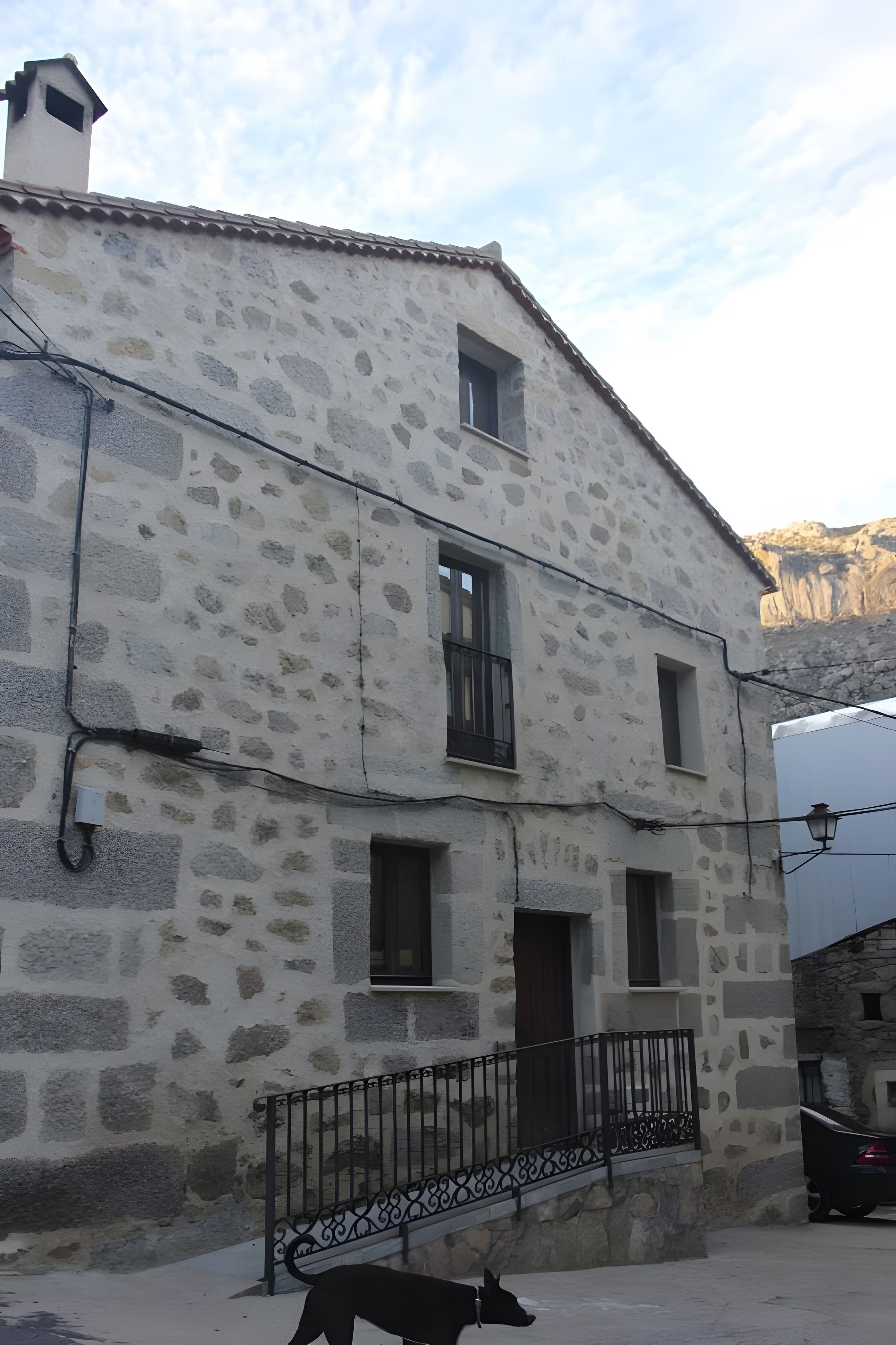 A two-story stone building with a balcony and a dog in front.