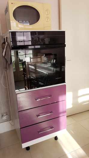 Una cocina con microondas, horno y un mueble de almacenamiento morado con cajones.