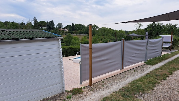 Un espacio exterior cercado con piscina, una zona de estar cubierta y un edificio con techo de tejas.
