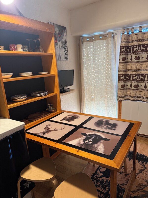A room with a wooden table displaying animal prints, a bookshelf with dishes, a computer, and a window with patterned curtains. - New Listing (Puyvalador)