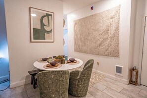 Un comedor con una mesa redonda, dos sillas tapizadas, un cuadro abstracto enmarco y un tapiz con textura.