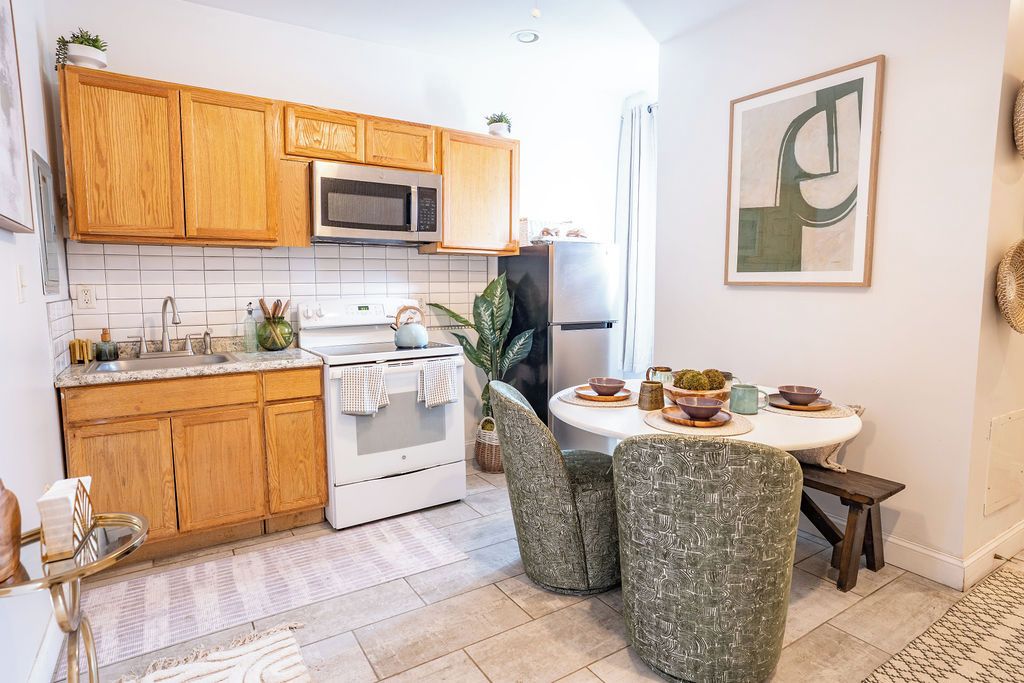A kitchen with wooden cabinets, a microwave, a stove, and a dining area with a table and chairs.