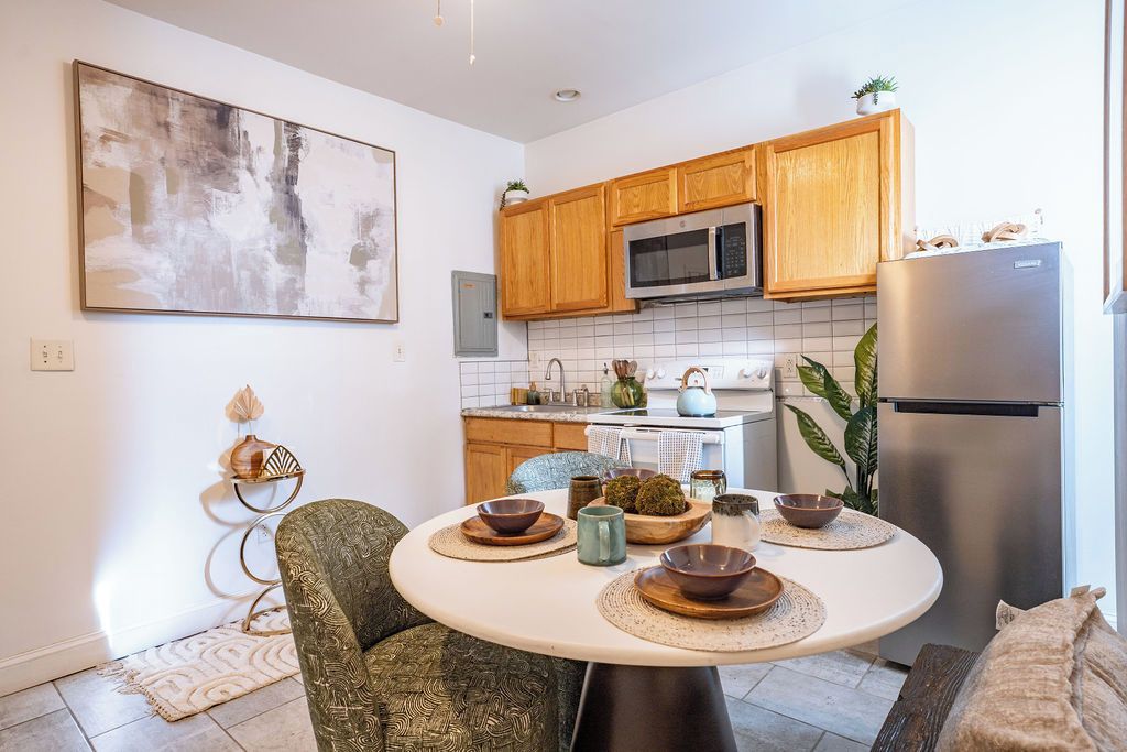 A modern kitchen with wooden cabinets, a stainless steel refrigerator, and a dining area with a round table.