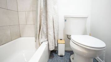 Un baño con bañera, inodoro y un cubo de basura.