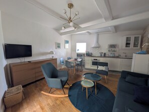 A modern living room with a flat-screen TV, a dining area with a table and chairs, a kitchenette with a microwave and stove, and a blue sofa. - New Listing (Teyran)