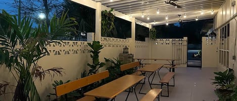 An outdoor patio area with multiple wooden benches and tables, a ceiling fan, and string lights.