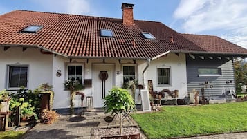 Een woonhuis met twee verdiepingen, een rode dakbedekking, een voortuin en een kleine tuin.