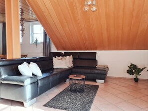 A modern living room with a black leather sofa, a round coffee table, and a wooden ceiling. - Apartment 'Am Lutherweg 1521' with Balcony and Wi-Fi (Breitenbach am Herzberg)