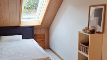 Een slaapkamer met een schuine kap, dakraam, een bed, een nachtkastje en een wandplank met manden.