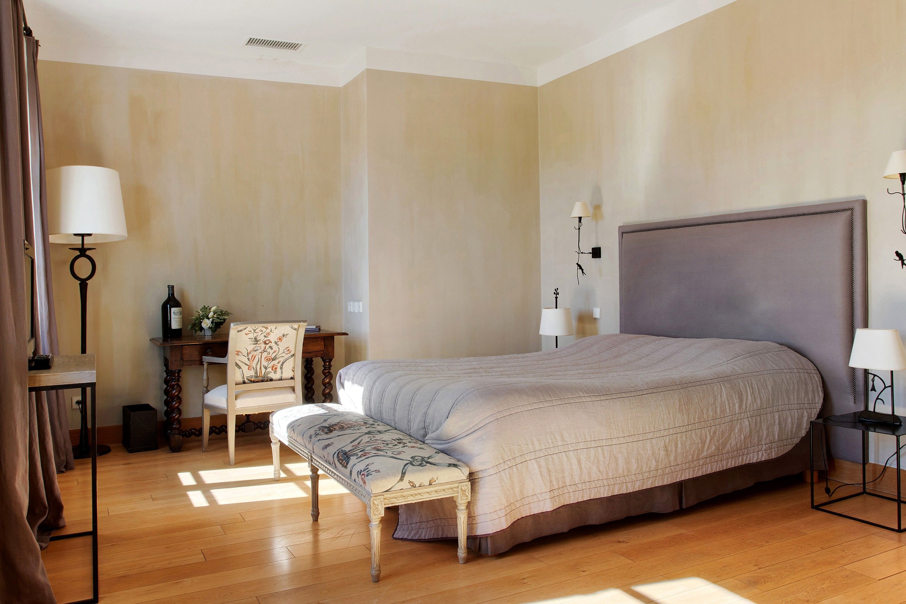 Ein Schlafzimmer mit einem großen Bett, einem Nachttisch, einem Sessel, einem Schreibtisch und einer Lampe.
