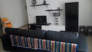 A living room with a black sofa, a television, and a decorative wall shelf.