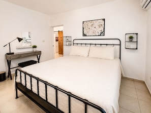 Un dormitorio con cama, mesita de noche, lámpara y repisa en la pared con una planta.