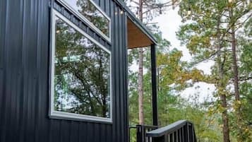 Een modern gebouw met een houten terras en metalen hekwerk, omgeven door bomen.
