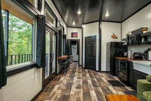 Cocina moderna con piso de madera en espiga, armarios negros y vistas al exterior a través de amplios ventanales.
