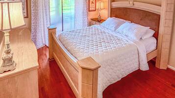A bedroom with a bed, bedside table, lamp, and a view of the outdoors.