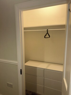 Um closet amplo com barra para pendurar roupas e várias gavetas.