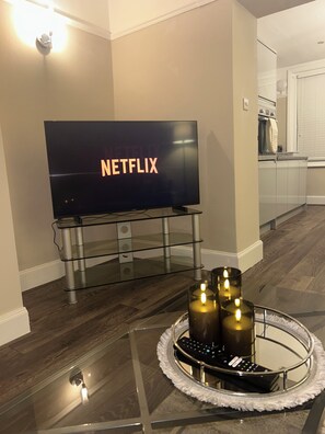 Uma sala de estar moderna com uma TV de tela plana exibindo o logotipo da Netflix, uma mesa de centro de vidro com velas e um controle remoto.