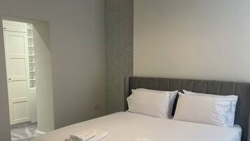 A neatly made bed with white linens and pillows, a grey upholstered headboard, and a chandelier above.
