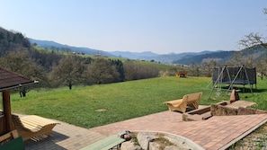 Eine Terrasse mit Gartenmöbeln, einer Schaukel und Blick auf ein grünes Feld und Berge.