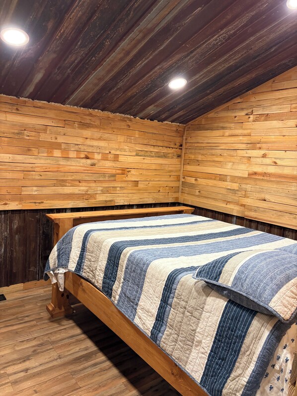 A wooden room with a bed, a bench, and a sloped ceiling. - Eagle Lake Hunting and Fishing Cabin (Vicksburg)