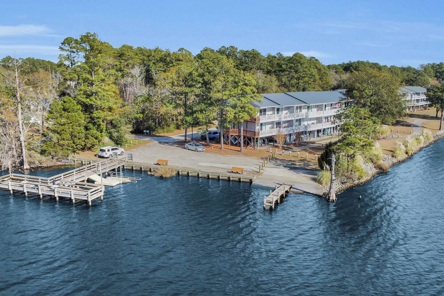 A waterfront property with a dock, a building with multiple balconies, and a parking area.
