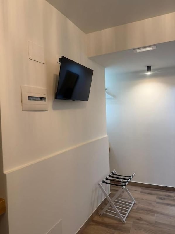 Un couloir avec un téléviseur à écran plat fixé au mur, un thermostat blanc également fixé au mur, et un étendoir à linge en métal.