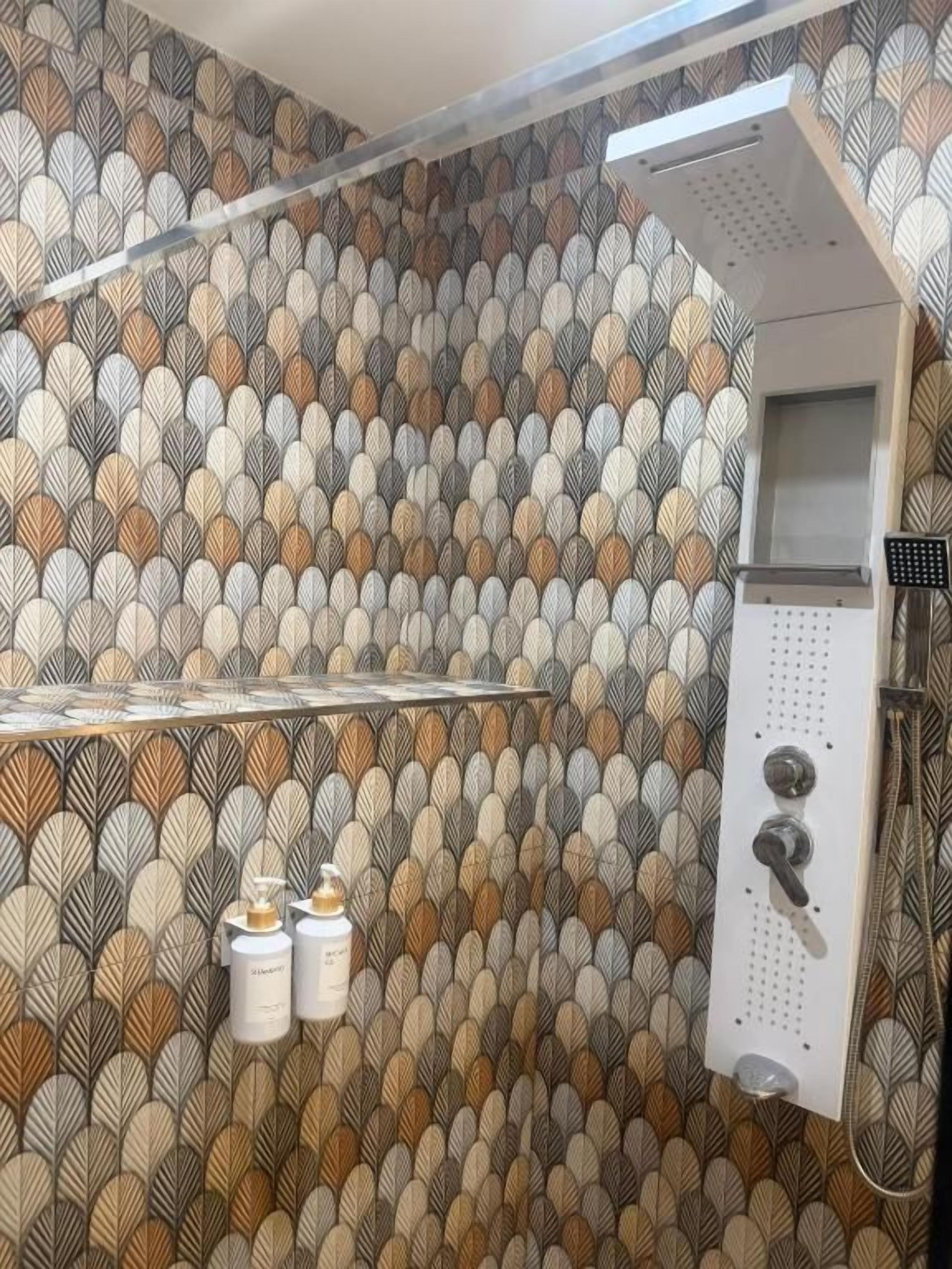 Bagno con parete decorata, zona doccia e due flaconi di shampoo.