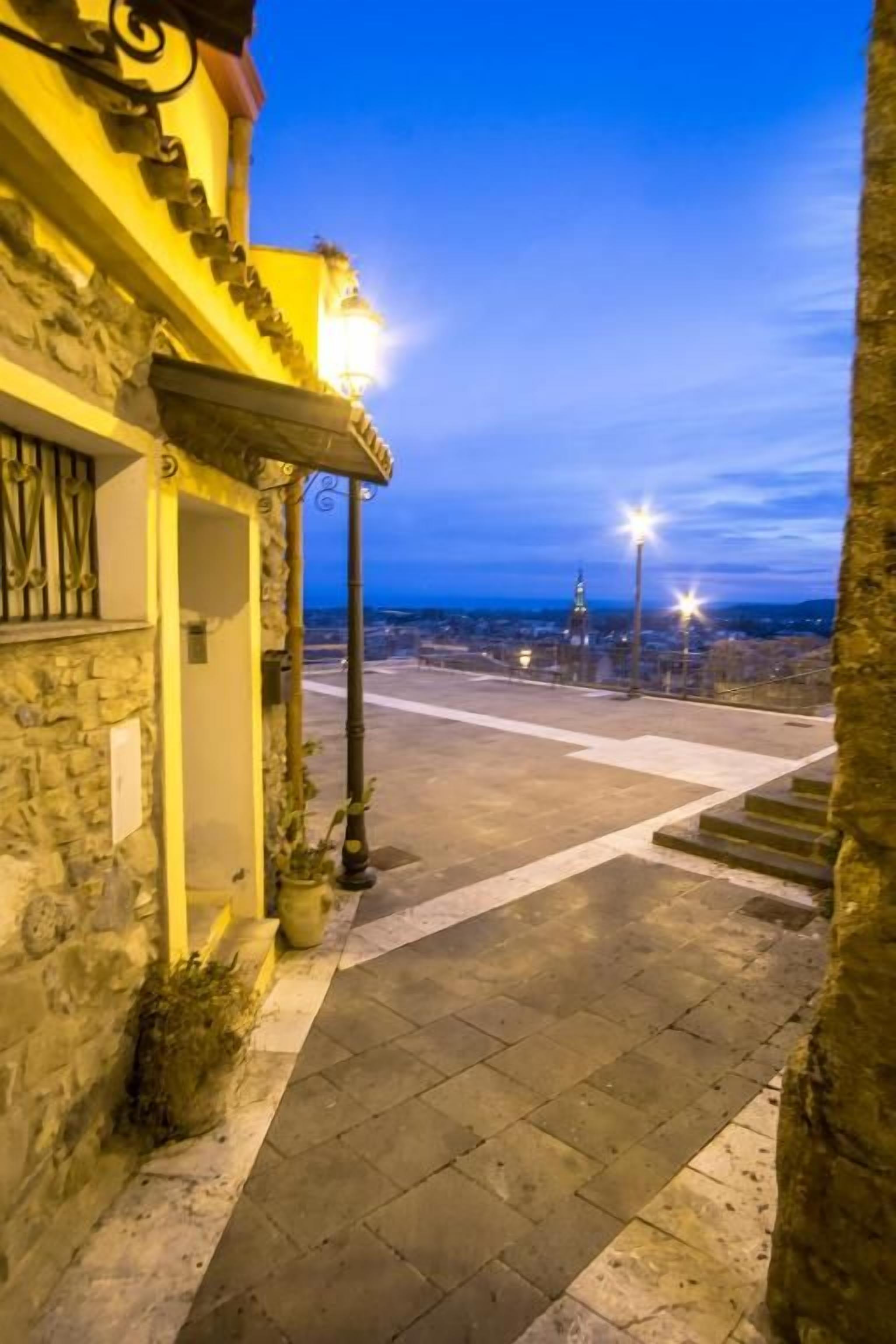 A stone building with a balcony, a street lamp, and a view of the cityscape at dusk.