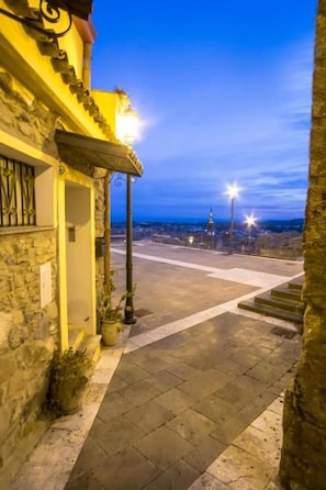 Un bâtiment en pierre doté d’un balcon, d’un lampadaire et offrant une vue sur le paysage urbain au crépuscule.